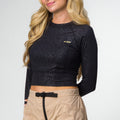 Woman wearing black Flex Performance Shirt with subtle pattern, long sleeves, and beige pants, front view showing logo on chest.
