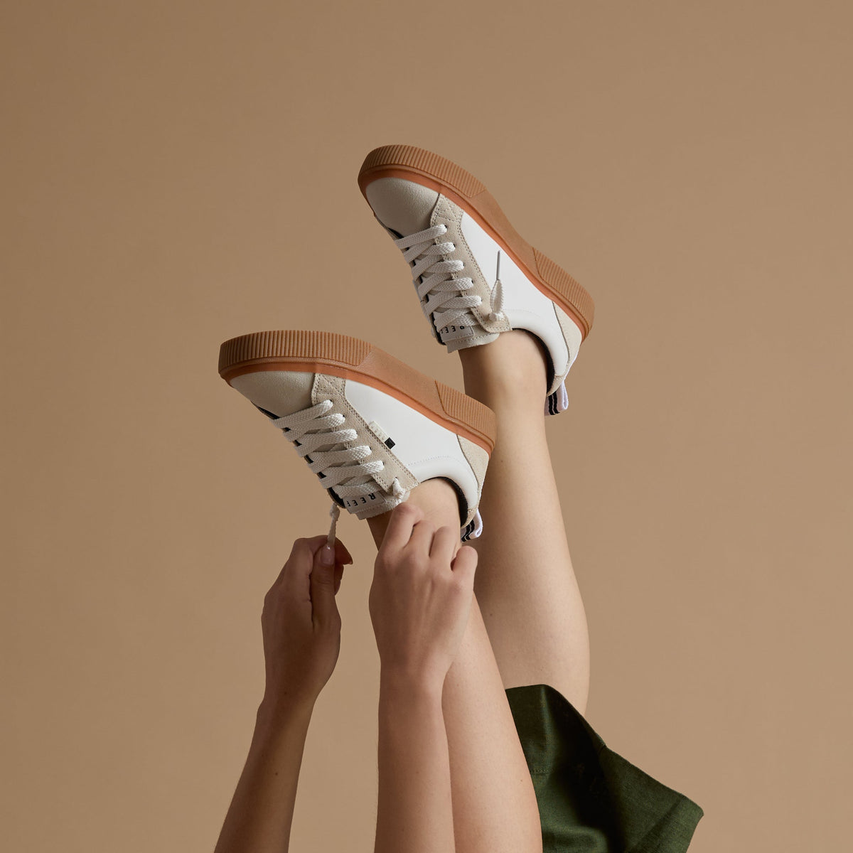 studio shot of woman wearing white and brown reef sneakers